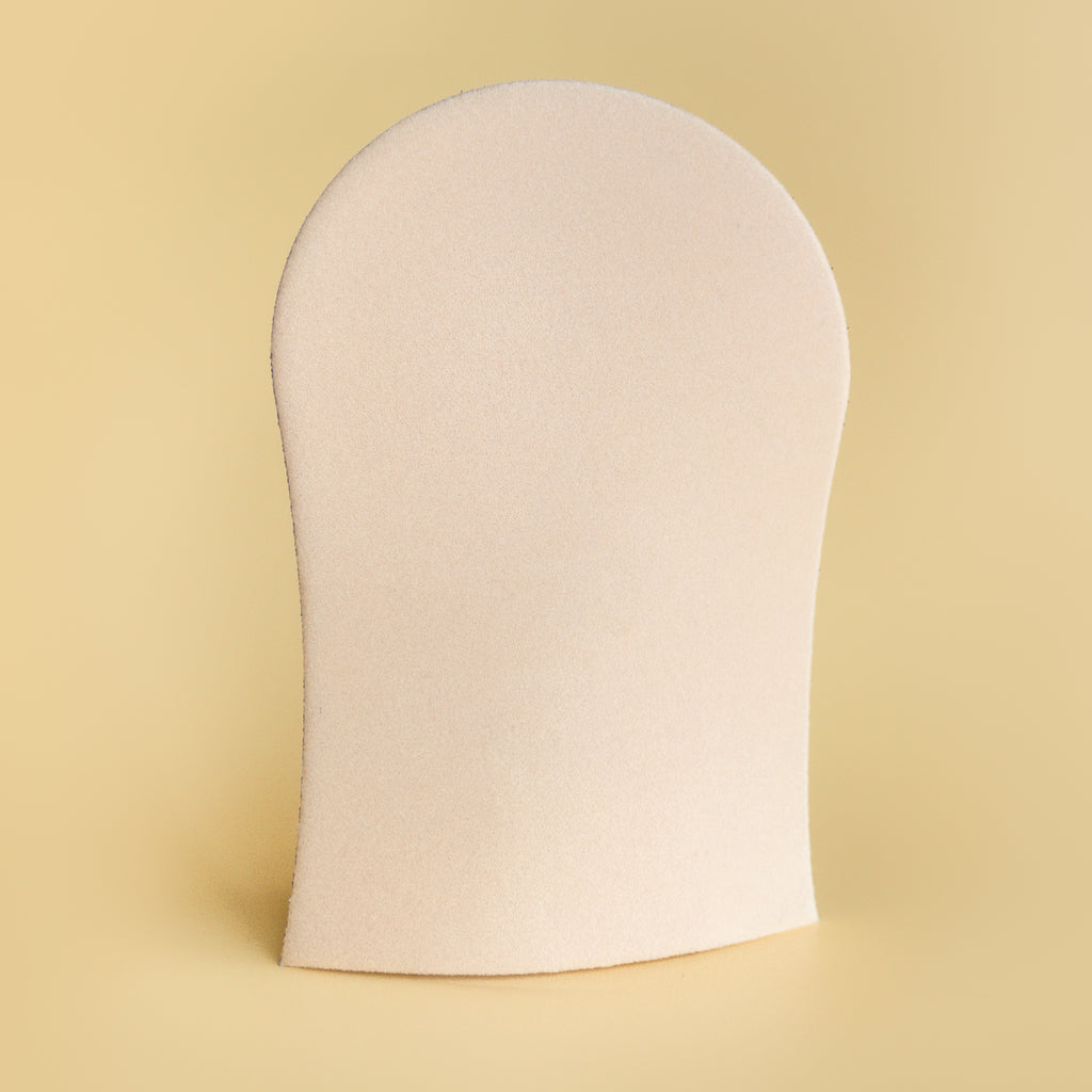 He-Shi GlowCare tanning mitt, machine washable, shown preventing stains while applying self-tanner on a hand.